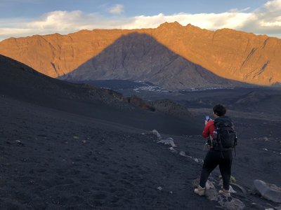 Ein Vulkan wirft einen Schatten, auf den eine Wanderin blickt