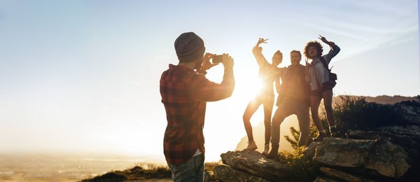 Ein Mann fotografiert eine Gruppe dreier Wanderer auf einem Berggipfel mit seinem Handy.