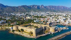Die Küstenstadt Girne Aus der Luft vom Meer aus schaut man auf die Küstenstadt Girne: Im Vordergrund liegen die Festung und der Hafen, dahinter erstreckt sich die Stadt, im Hintergrund erheben sich Berge.
