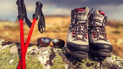 Auf einem Felsen abgestellte Wanderstöcke, Sonnenbrille und Wanderschuhe.