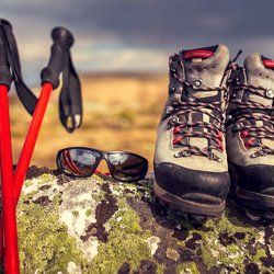 Auf einem Felsen abgestellte Wanderstöcke, Sonnenbrille und Wanderschuhe.