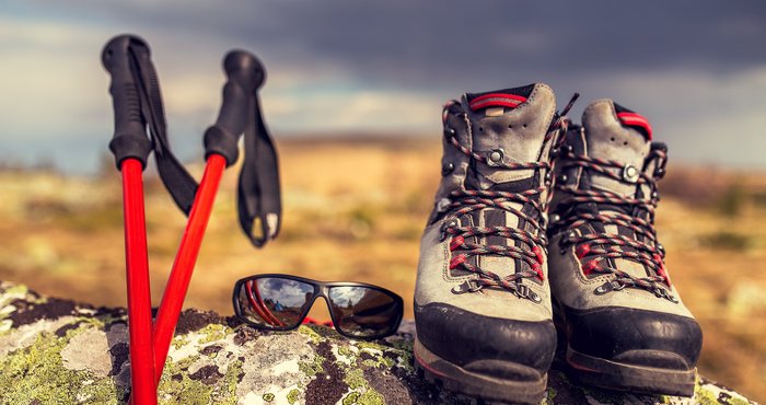 Auf einem Felsen abgestellte Wanderstöcke, Sonnenbrille und Wanderschuhe.