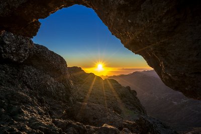 Aus einer Felshöhle in der Gebirgslandschaft Gran Canarias erblickt man die aufgehende Sonne.