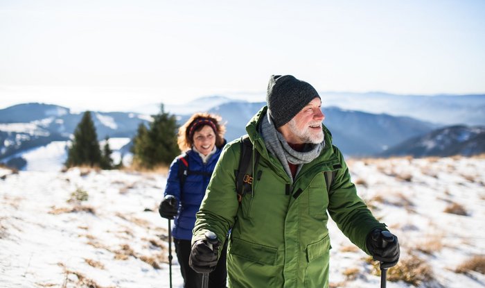 Ein älteres Paar wandert mit Wanderstöcken ausgestattet durch eine Gebirgslandschaft.