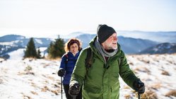 Ein älteres Paar wandert mit Wanderstöcken ausgestattet durch eine Gebirgslandschaft.