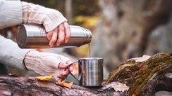 Eine Frau gießt Wasser aus einer Thermoskanne im Wald.