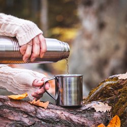 Eine Frau gießt Wasser aus einer Thermoskanne im Wald.