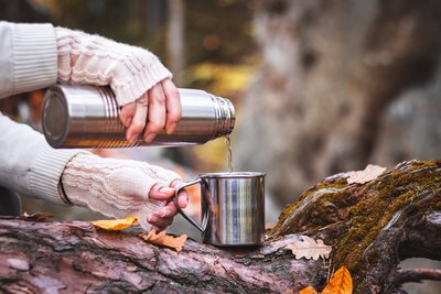 Eine Frau gießt Wasser aus einer Thermoskanne im Wald.