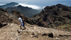 Eine einsame Wanderin beschreitet einen Pfad im Gebirge oberhalb des Meeres von La Palma.