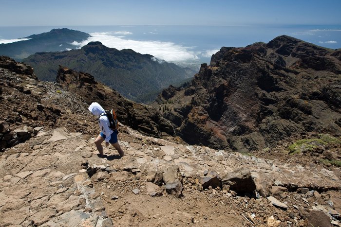 Eine einsame Wanderin beschreitet einen Pfad im Gebirge oberhalb des Meeres von La Palma.