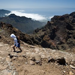 Eine einsame Wanderin beschreitet einen Pfad im Gebirge oberhalb des Meeres von La Palma.