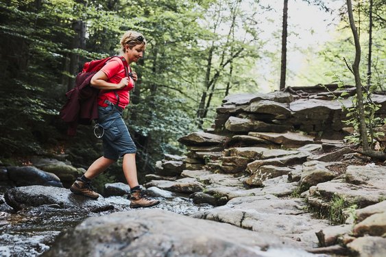 Bloß keine nassen Füße kriegen! Eine Wanderin überquert einen Bach im Wald