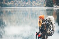 Eine Wanderin mit Mütze, Handschuhen und Rucksack steht vor einem See im Winter