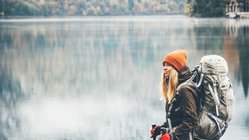 Eine Wanderin mit Mütze, Handschuhen und Rucksack steht vor einem See im Winter