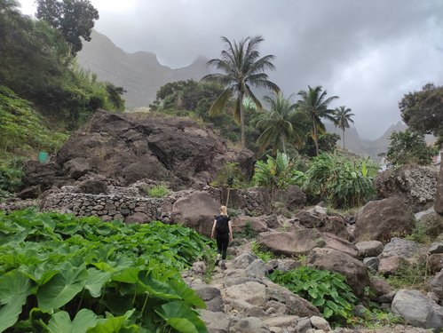 Zwischen üppig-grüner Vegetation und grauem Felsgestein erklimmt eine blonde Frau einen Berg auf dem kapverdischen Wanderparadies Santo Antão.