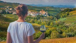 Eine Frau blickt auf Weinterrassen im Piemont mit einem Glas Rotwein in der Hand