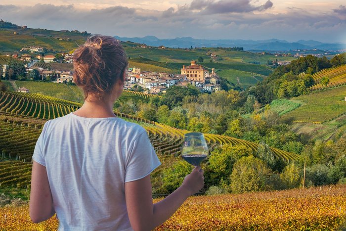 Eine Frau blickt auf Weinterrassen im Piemont mit einem Glas Rotwein in der Hand