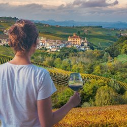 Eine Frau blickt auf Weinterrassen im Piemont mit einem Glas Rotwein in der Hand