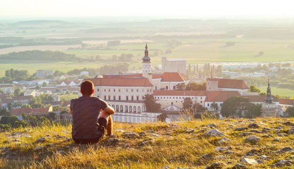 Ein Mann sitzt auf einem Hügel und blickt auf Schloss Mikulov im Tal vor ihm.