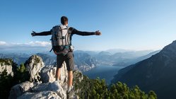 Wanderfreiheit über dem Gardasee Ein Wanderer steht mit weit ausgebreiteten Armen im Gebirge über dem Gardasee und schaut hinunter.