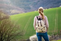 Man sieht die Rückensicht einer Frau it Wanderrucksack, die vor einem Feld steht.