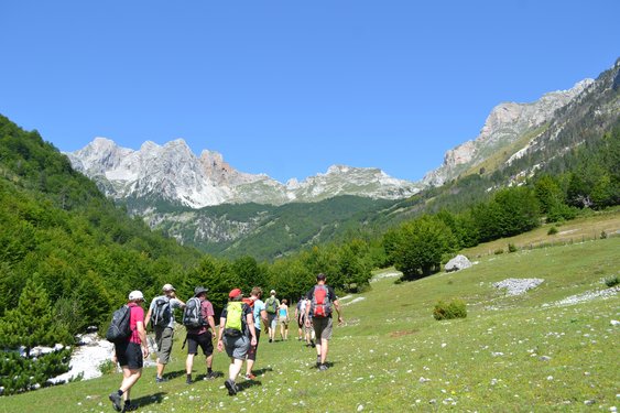 Eine Wandergruppe läuft über eine Wiese entgegen dem imposanten Alpenpanorama in Albanien.