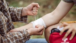 Erste Hilfe bei Wanderungen Ein Wanderer bekommt den Arm mit einer Mullbinde verbunden