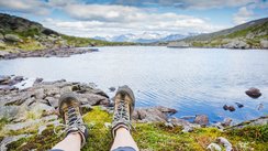 Man sieht die ausgestreckten Beine eines Wanderers bei der Rast an einem Seeufer.