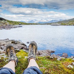 Man sieht die ausgestreckten Beine eines Wanderers bei der Rast an einem Seeufer.
