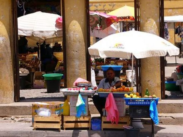 Verkäufer sitzt an seinen aus Kisten aufgebauten Obststand