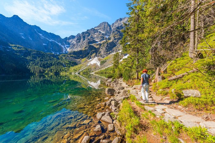 Eine Frau wandert entlang eines glasklaren Bergsees zwischen den Bergen der Hohen Tatra.