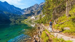 Eine Frau wandert entlang eines glasklaren Bergsees zwischen den Bergen der Hohen Tatra.