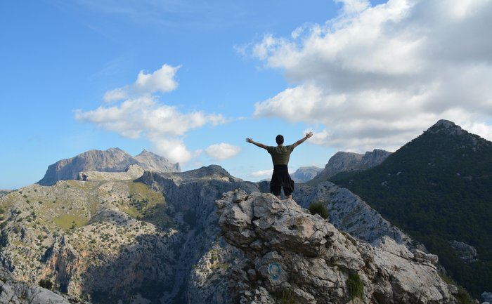 Ein Wanderer reckt die Arme bei einer Gipfelwanderung auf Mallorca.