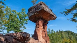 Die Felsformation Teufelstisch im Pfälzerwald ragt hinaus in einen leuchtend blauen Himmel.