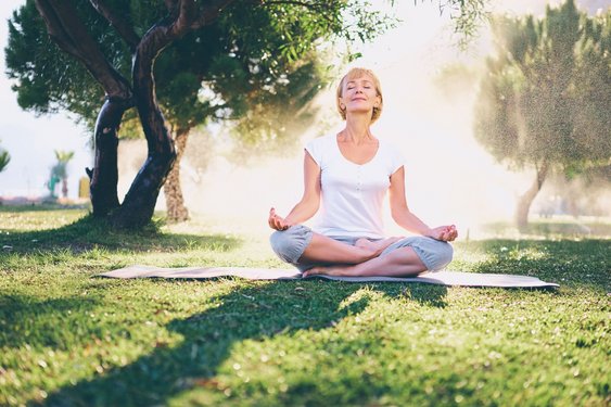 Aktive Entspannung durch Yoga Eine Frau sitzt im Lotussitz in einem Park und entspannt sich.