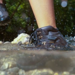 Eine Wanderin läuft mit ihren Wanderstiefeln durch einen Bach