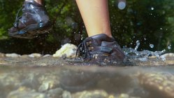 Wandern durch einen Bach Eine Wanderin läuft mit ihren Wanderstiefeln durch einen Bach