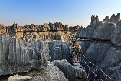 Zwei Wanderer überqueren eine Schlucht über eine Hängebrücke in den Tsingy de Bemaraha auf Madagaskar